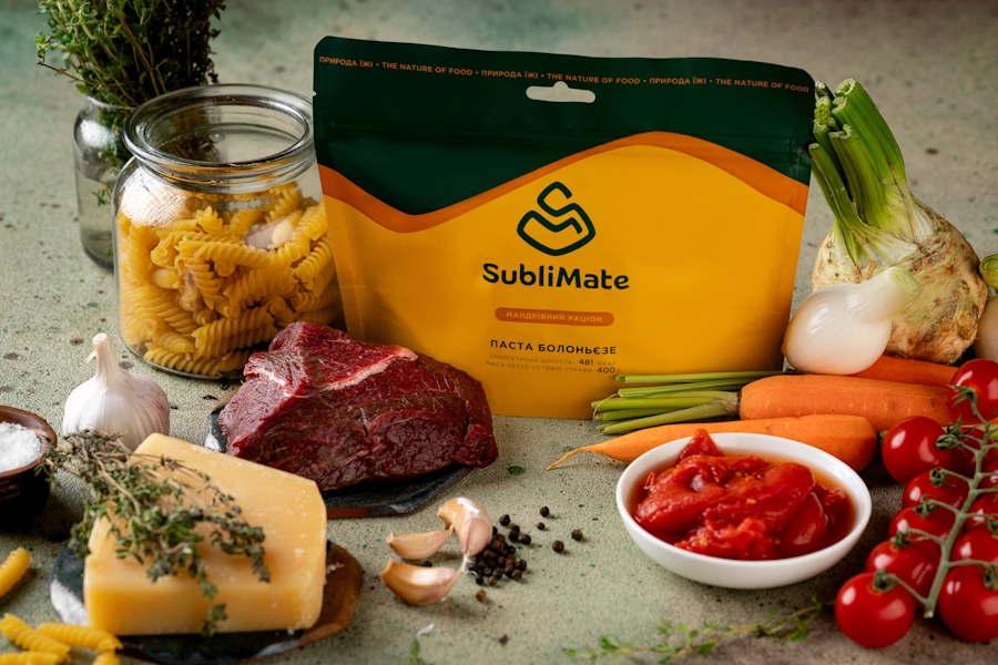 Складові пасти болоньєзе SubliMate на столі: сухі макарони, яловичина, овочі, сир, спеції та брендована упаковка