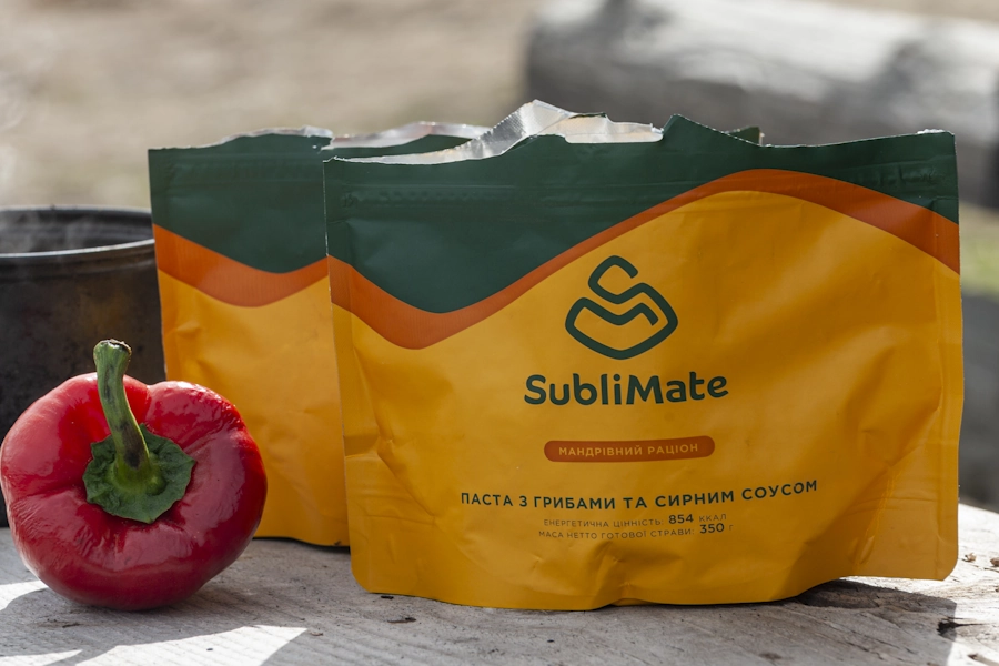 Жовто-зелене пакування пасти Sublimate на сонці, поряд червоний перець і казанок на фоні природи